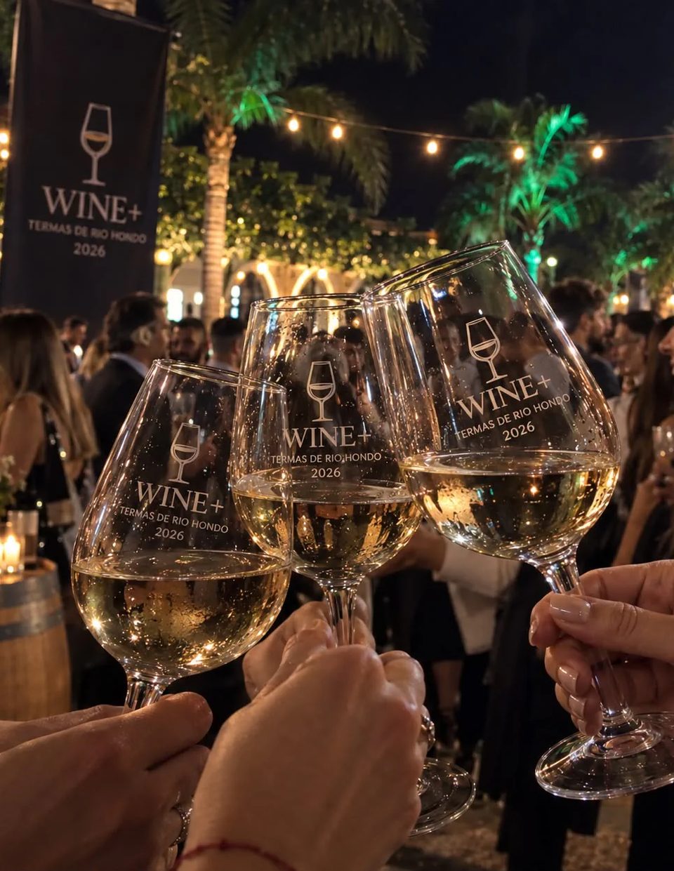 Brindis con copas de vino WINE+ en una fiesta nocturna, con luces de guirnalda y un banner de WINE+ de fondo